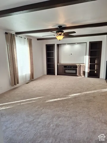 Recessed entertainment center with built-in shelving, decorative ceiling beams, ceiling fan with integrated lighting, and neutral-toned carpeting