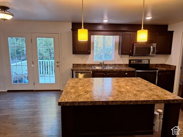 Kitchen featuring an island with a patterned countertop, dark wood-finish cabinetry, stainless steel appliances, and wood-finish flooring