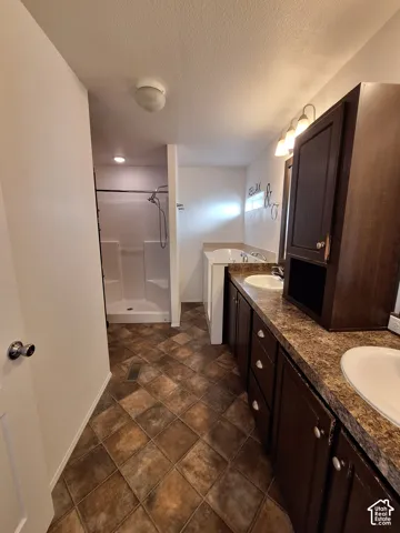 Dual vanity with dark wood-finish cabinetry, a drop-in soaking tub, a stand-up shower, and patterned floor tiling