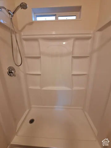 Spacious shower enclosure featuring a seamless acrylic surround with built-in shelving, chrome showerhead with handheld attachment, and a slip-resistant floor with integrated drain
