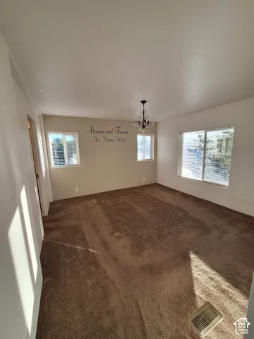 Spacious room featuring broadloom carpeting, multiple windows with blinds, and a decorative chandelier