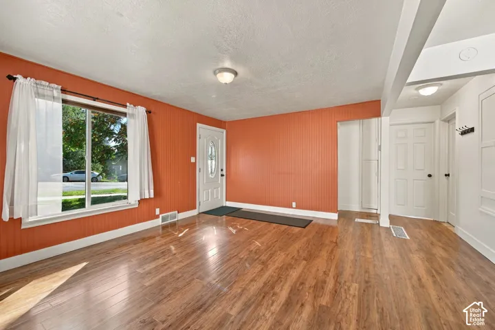 Wood-finish flooring throughout, white trim, and a white entry door with a decorative glass insert