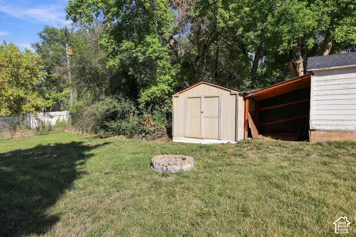 Expansive green lawn with a paver fire pit, storage shed, and an additional covered outdoor structure