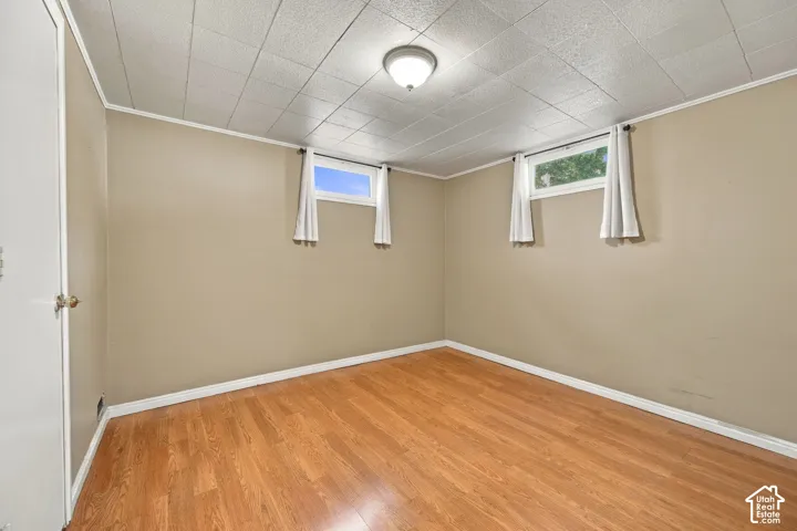Bright basement room with warm wood-finish flooring, crisp white trim, and soft beige walls