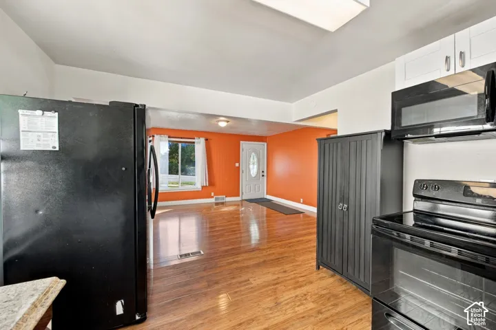 Wood-finish flooring, white overhead cabinetry, black over-the-range microwave, and a black electric range