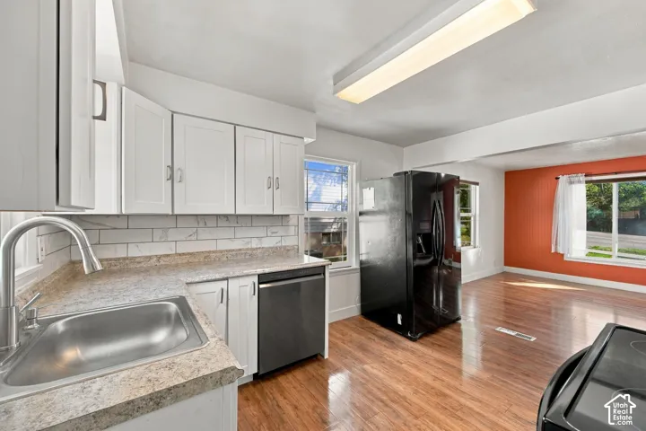 White shaker cabinetry, stainless steel sink, wood-finish flooring, black refrigerator, and built-in dishwasher