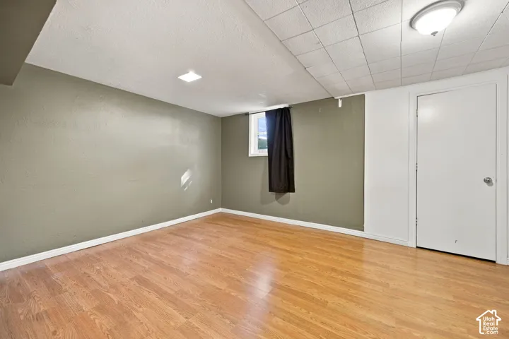 Spacious room featuring wood-finish flooring, neutral-toned walls, a drop ceiling, and an egress window