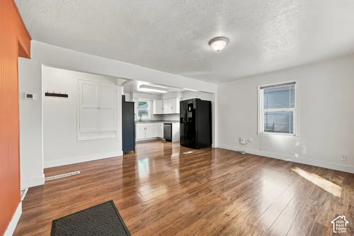 Wood-finish flooring throughout, white walls, and a recessed kitchen with white cabinetry