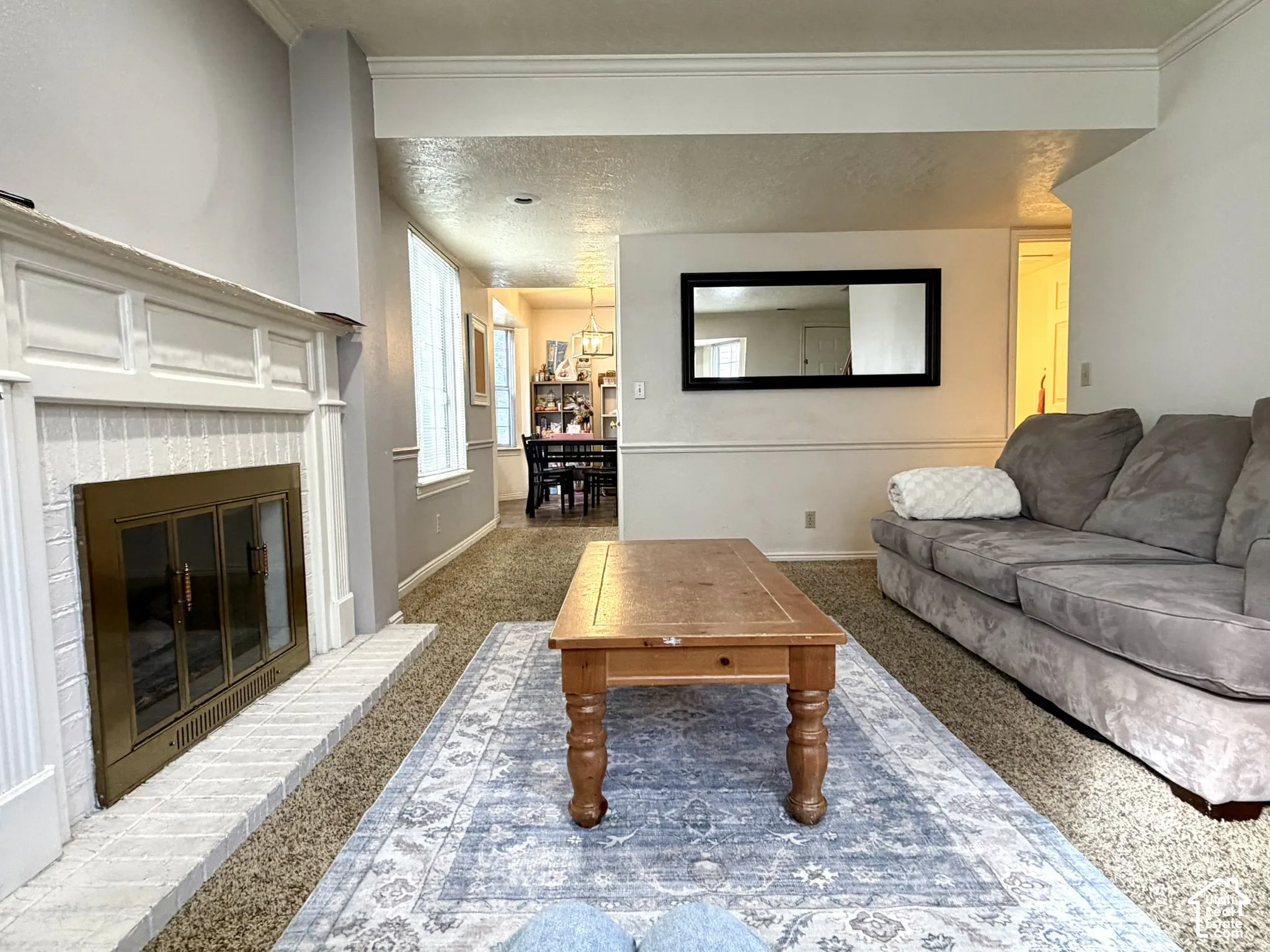 Living area featuring a white brick fireplace with a brass firebox, and neutral-toned carpeting