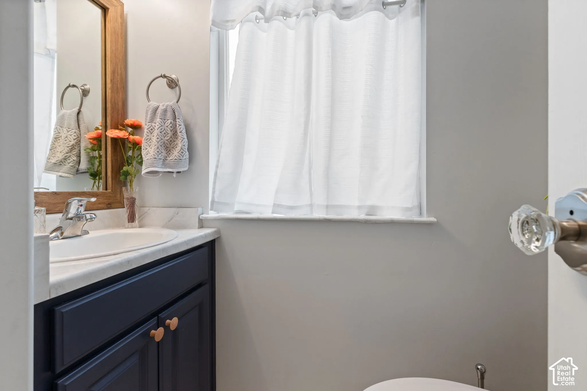 Bathroom featuring a dark wood-finish vanity with a white countertop, a wood-framed mirror, and a window with natural light
