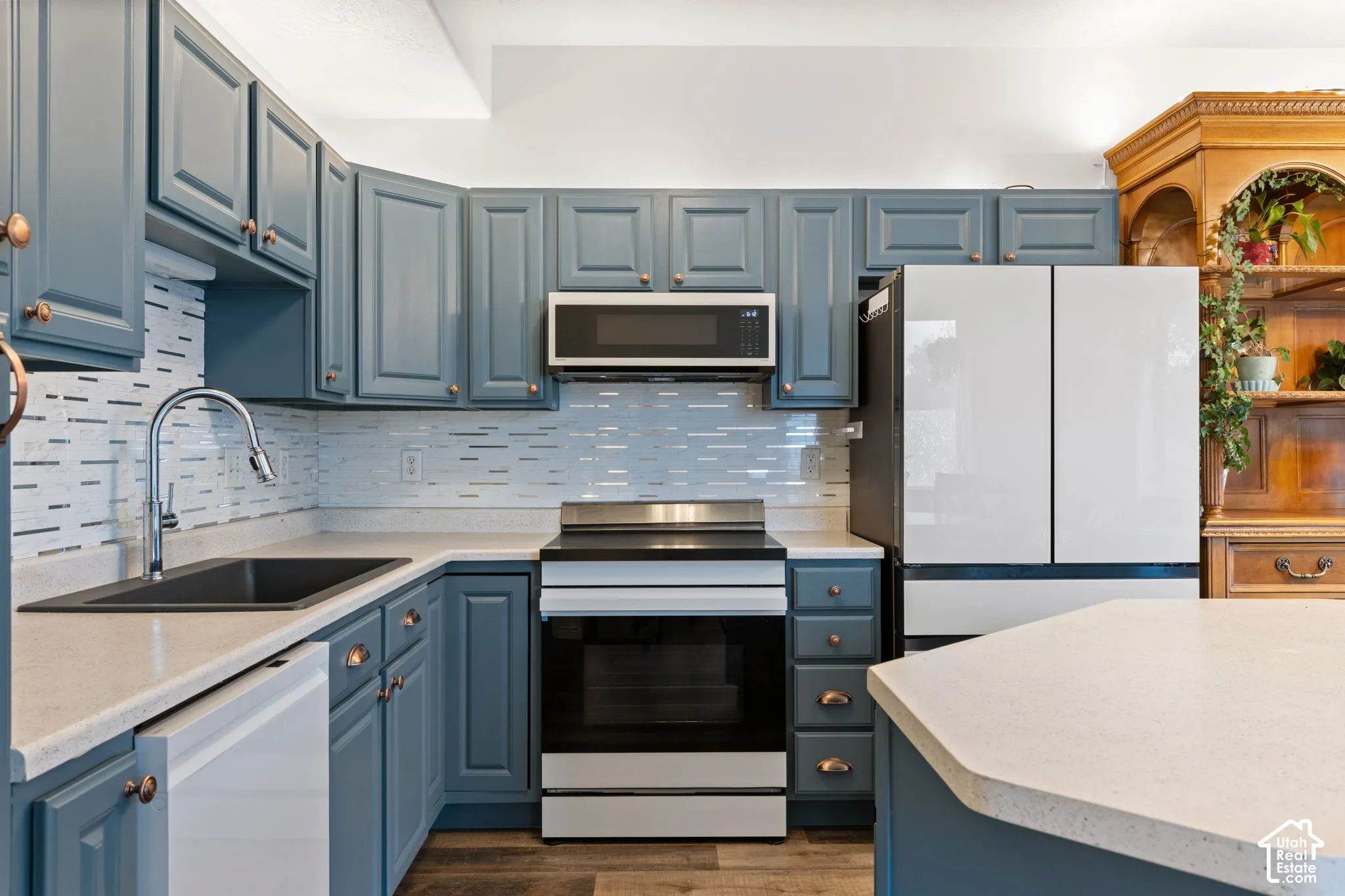 Blue shaker-style cabinetry with copper-toned hardware, light-toned countertops, tile backsplash, and stainless steel appliances