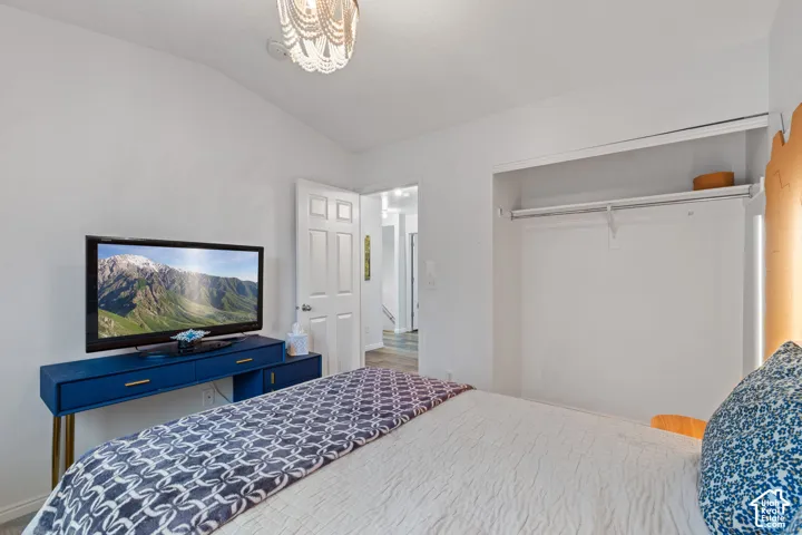 Vaulted ceiling, white painted walls, wood-finish flooring, built-in closet with shelving and hanging rod, and a six-panel interior door