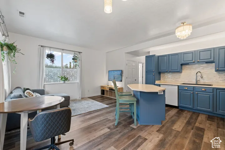 Open-concept living space with wood-finish flooring, a kitchen island with seating, blue cabinetry, and a tile backsplash