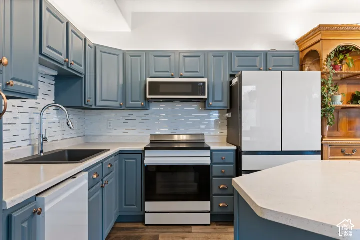 Blue shaker-style cabinetry with copper-toned hardware, light-toned countertops, tile backsplash, and stainless steel appliances