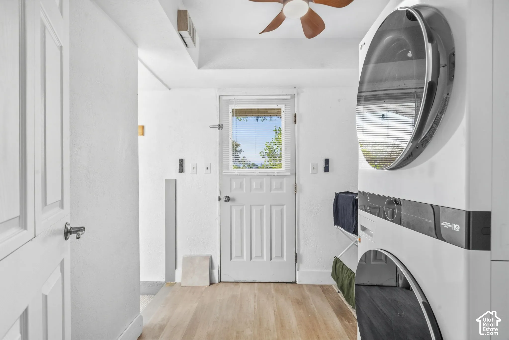 Laundry area featuring a stacked washer and dryer, wood-finish flooring, a white paneled door with window, and a ceiling fan