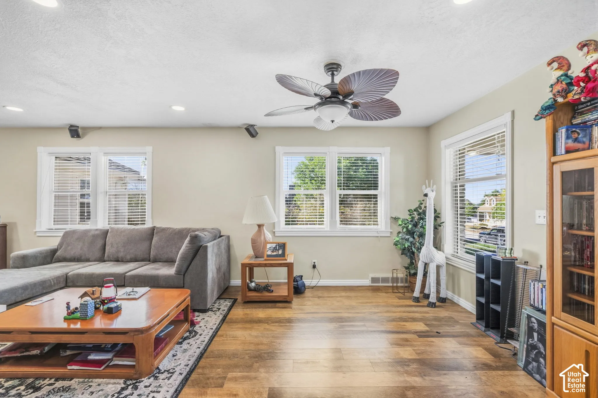 Recessed ceiling lighting, wood-finish flooring, multiple windows with blinds, a ceiling fan, and built-in shelving