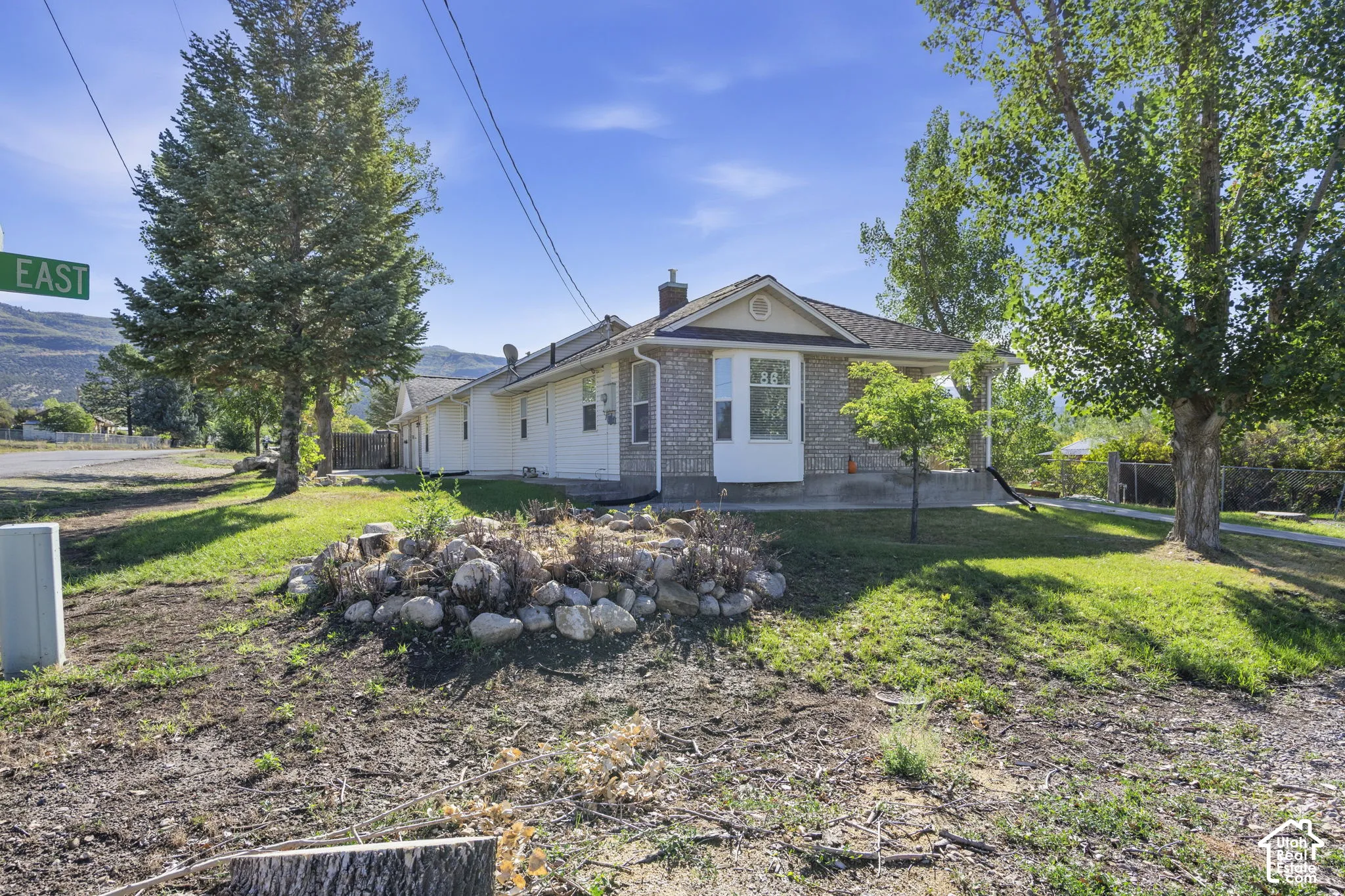 Brick and siding exterior featuring a bay window, mature trees, and a sloped lawn