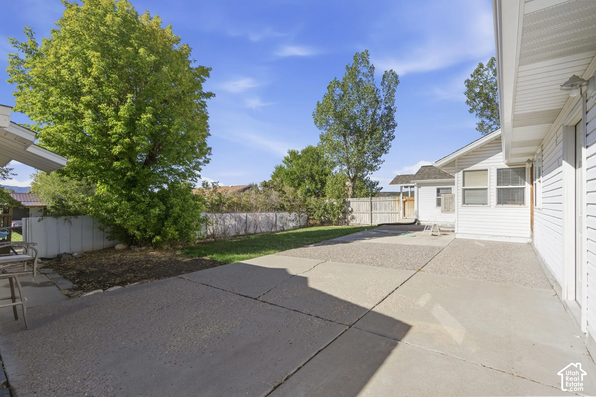 Expansive concrete patio with a grassy area and mature trees