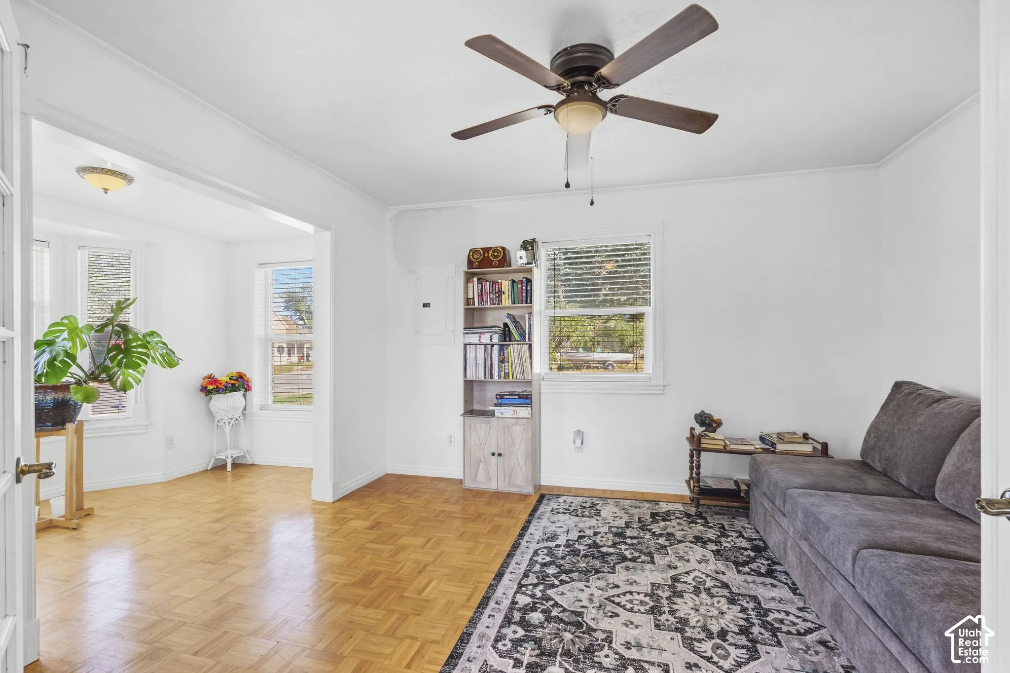 Light-filled interior space featuring wood-finish flooring, a ceiling fan with integrated lighting, multiple windows, and a built-in bookshelf