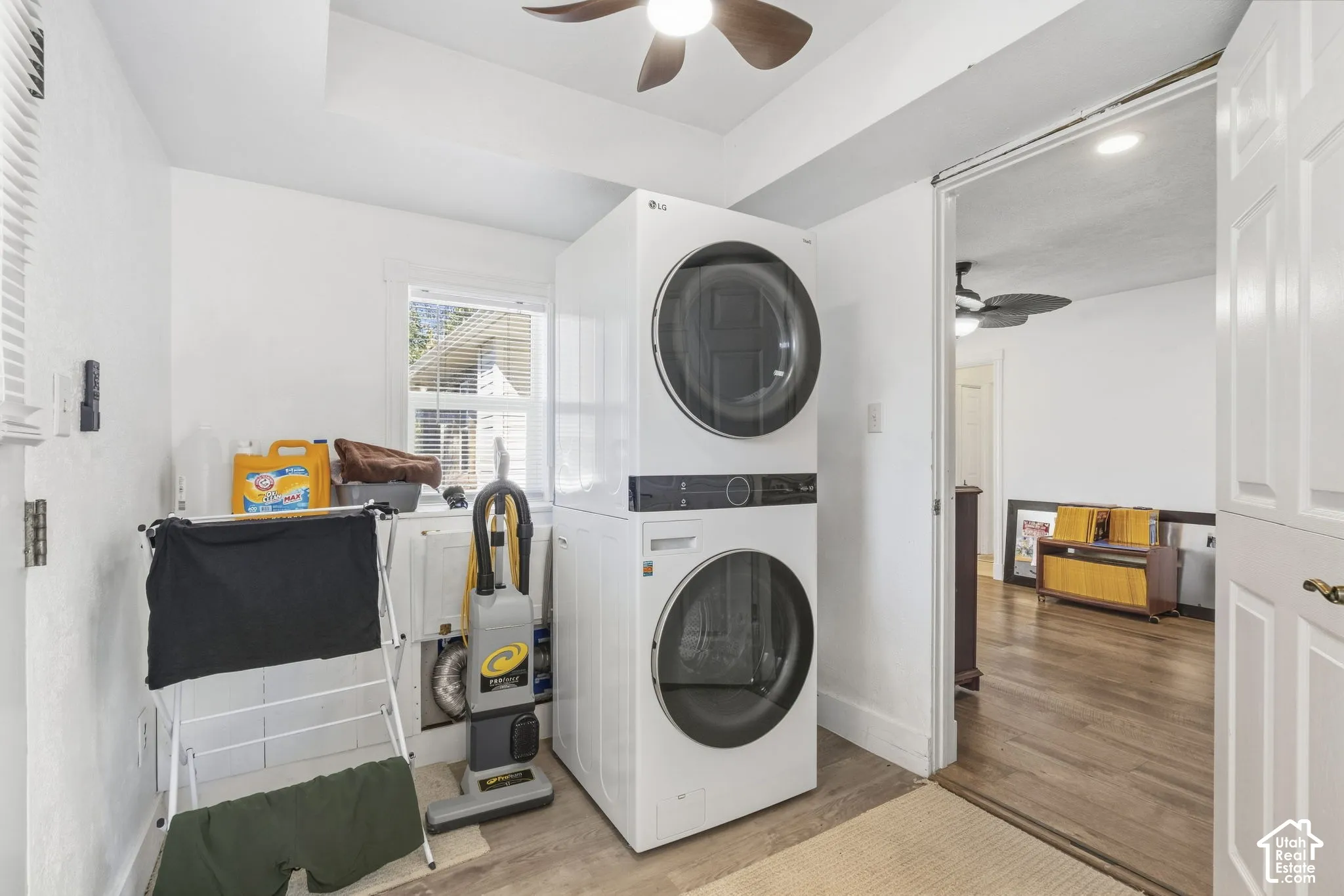 Dedicated laundry room featuring stackable front-load washer and dryer with modern white finish, wood-finish flooring, ceiling fan, and ample storage cabinetry