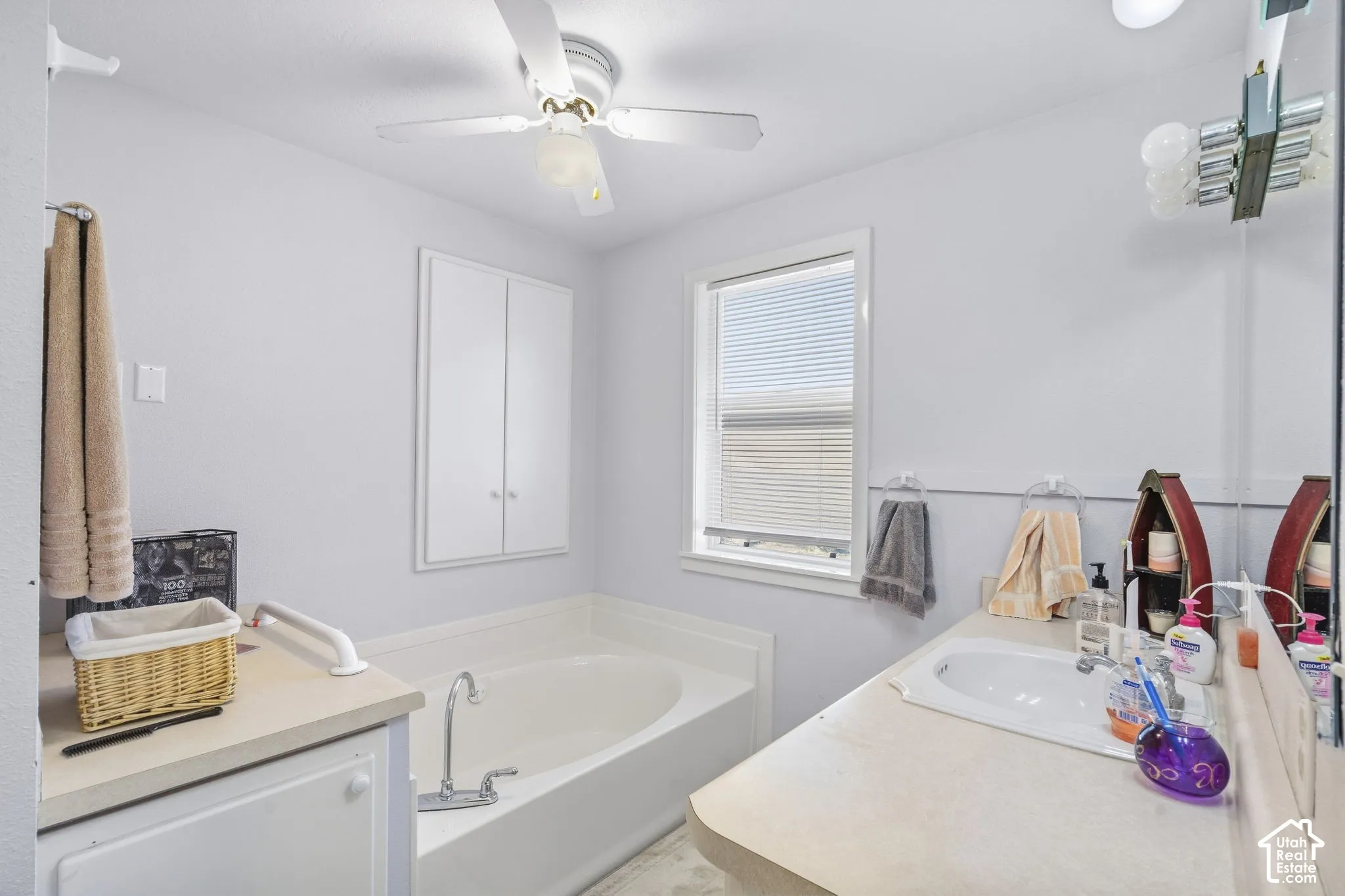 Bathtub with a deck-mounted faucet, built-in wall cabinet, vanity with an integrated sink, vanity mirror, and overhead ceiling fan with lighting