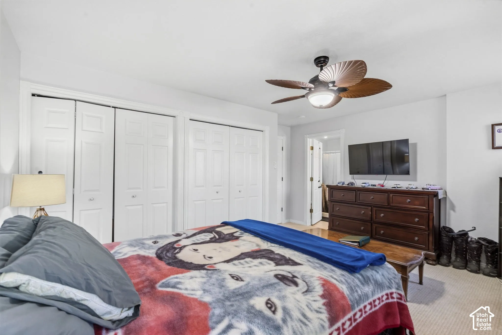 Wall-mounted ceiling fan with integrated lighting, multiple white bi-fold closet doors, and light-toned carpet flooring