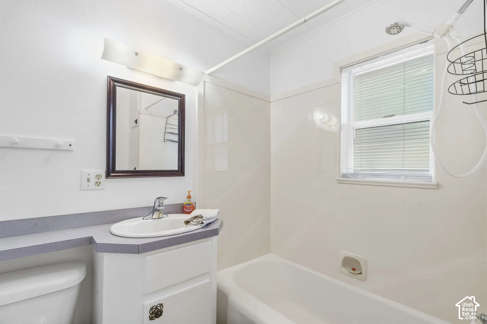 Single window with blinds, vanity with an integrated sink, shower-over-tub combination, and a wall-mounted mirror