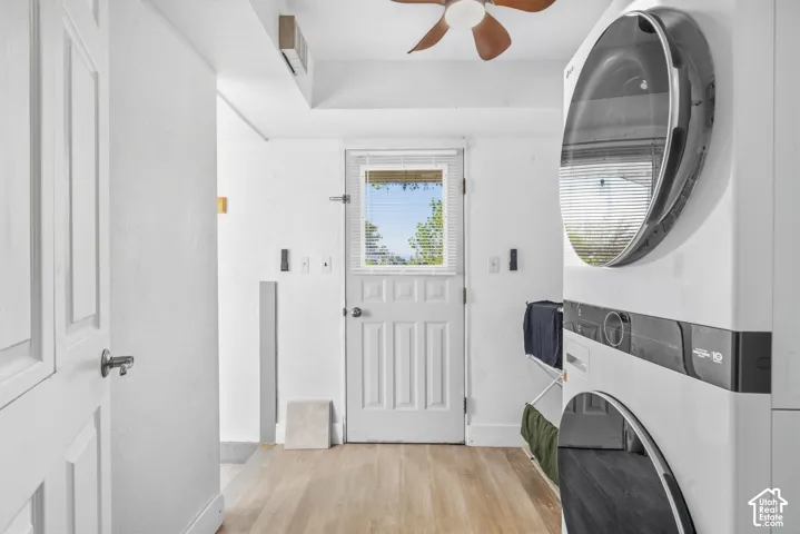 Laundry area featuring a stacked washer and dryer, wood-finish flooring, a white paneled door with window, and a ceiling fan