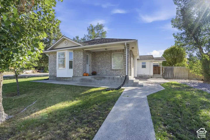 Charming brick residence featuring a covered front entrance, manicured lawn with mature landscaping, concrete walkway, and detached garage