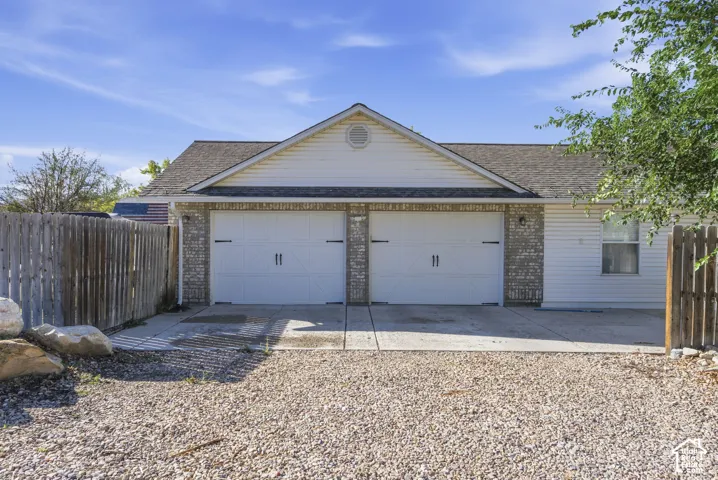 Two-car garage with white doors, brick veneer detailing, and a gravel driveway