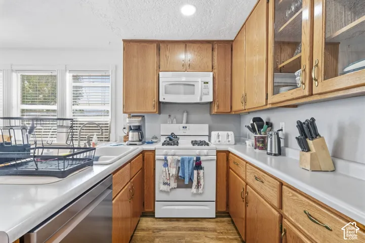 Kitchen featuring wood-finish cabinetry, white countertops, built-in microwave, integrated dishwasher, and a window above the sink