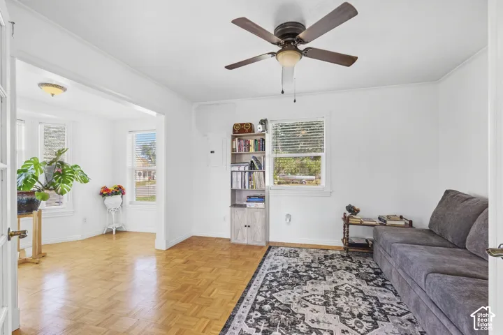 Light-filled interior space featuring wood-finish flooring, a ceiling fan with integrated lighting, multiple windows, and a built-in bookshelf