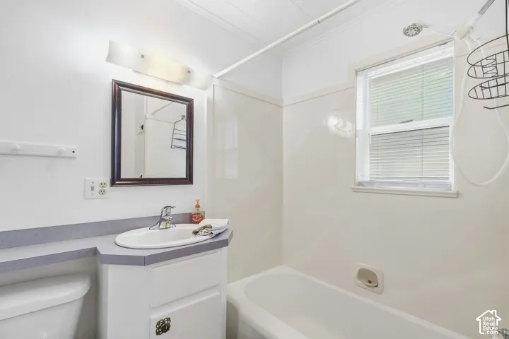 Single window with blinds, vanity with an integrated sink, shower-over-tub combination, and a wall-mounted mirror
