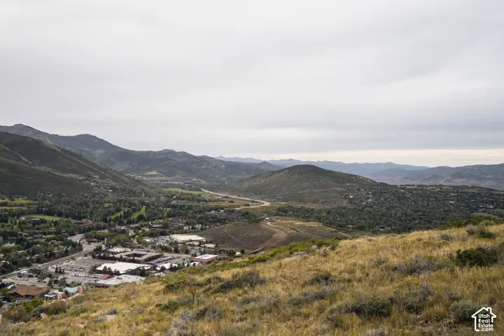 Expansive landscape featuring distant mountains, a valley with established communities, and a prominent roadway