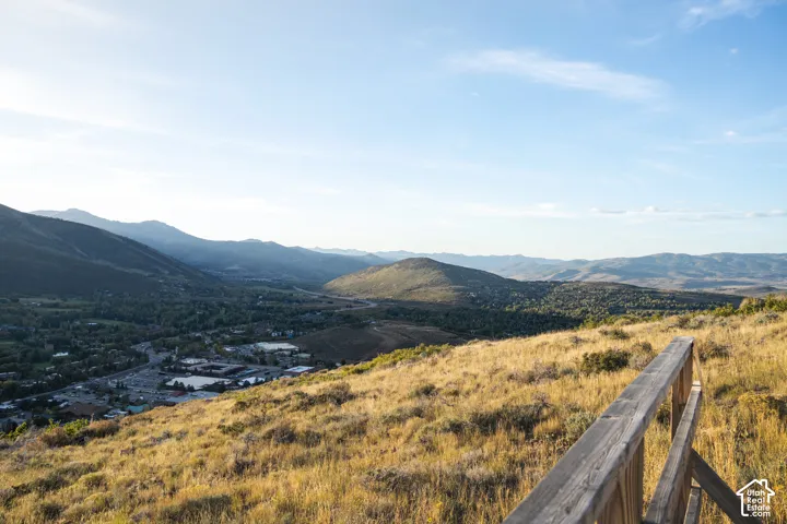 Expansive mountain terrain, distant valley, scattered structures, and a wooden railing