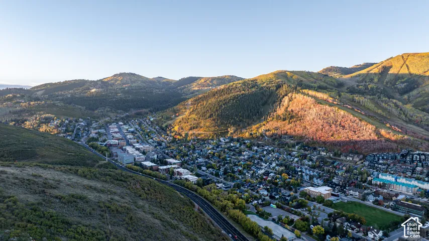 Expansive mountain landscape featuring a valley with residential and commercial structures, surrounded by wooded hillsides