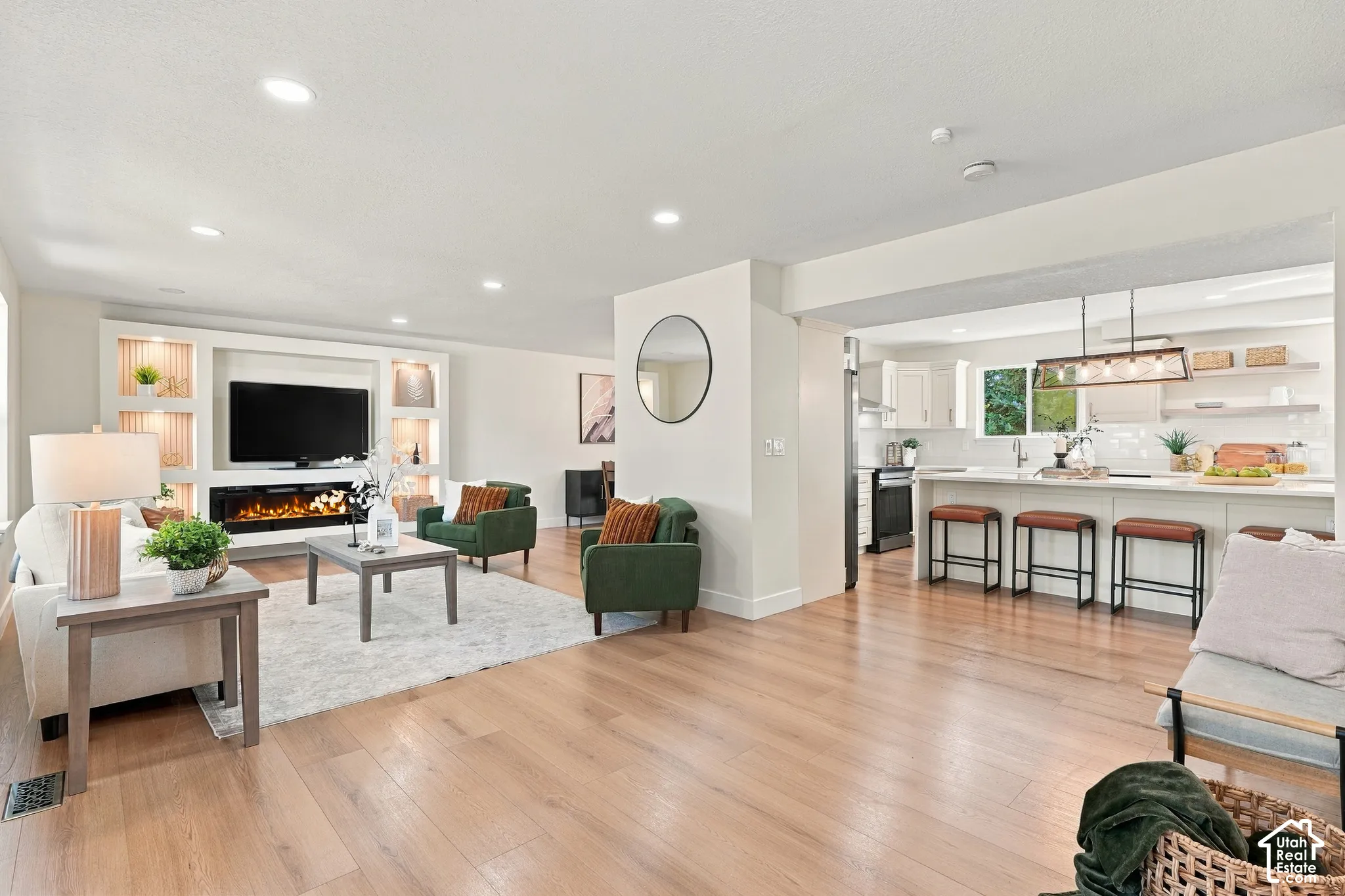 Light wood-finish flooring throughout, recessed ceiling lighting, and a built-in media console with an electric fireplace