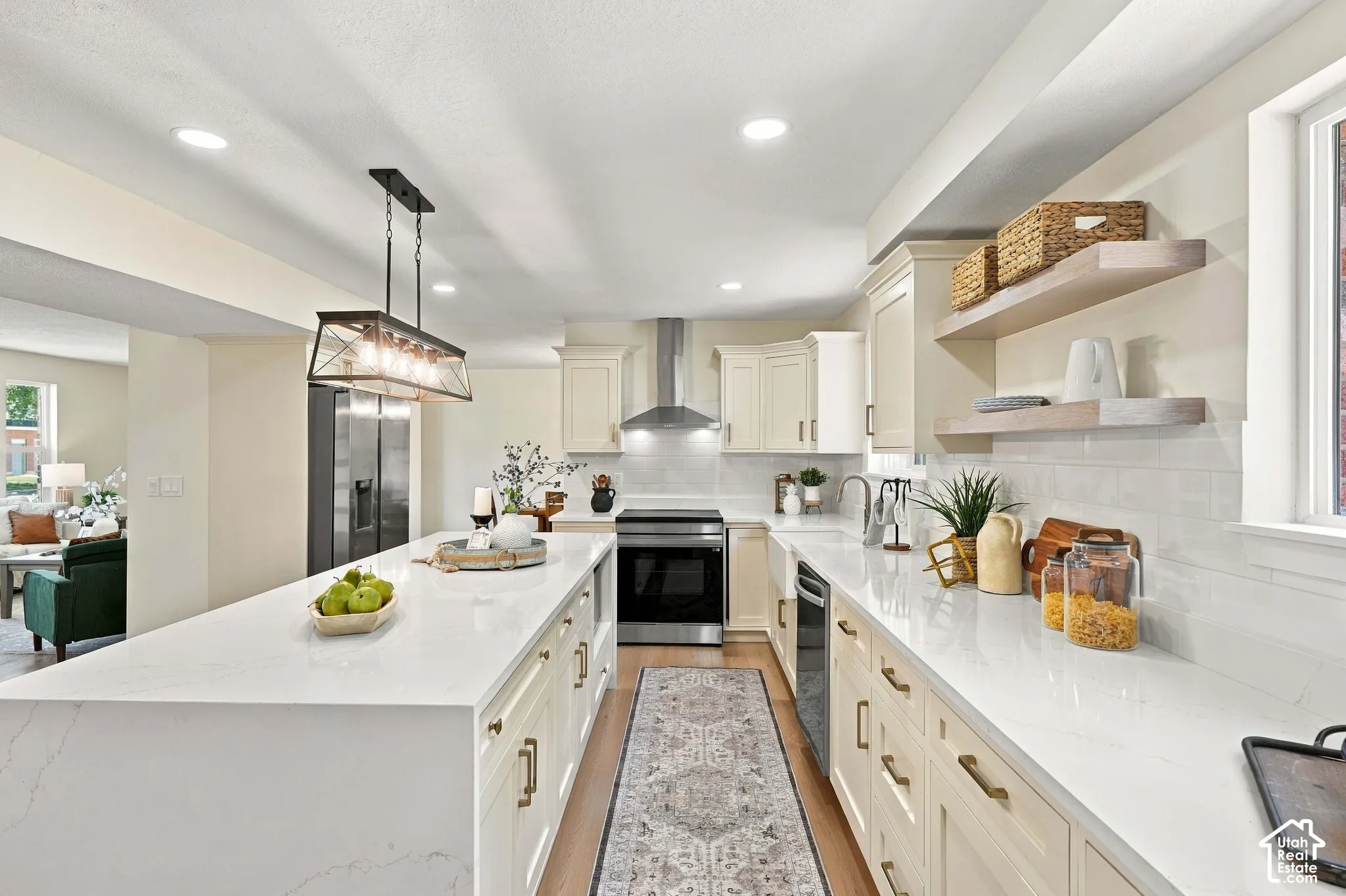Kitchen featuring a large island with a waterfall countertop, recessed lighting, wood-finish flooring, a stainless steel appliance suite, and light-toned cabinetry with gold hardware