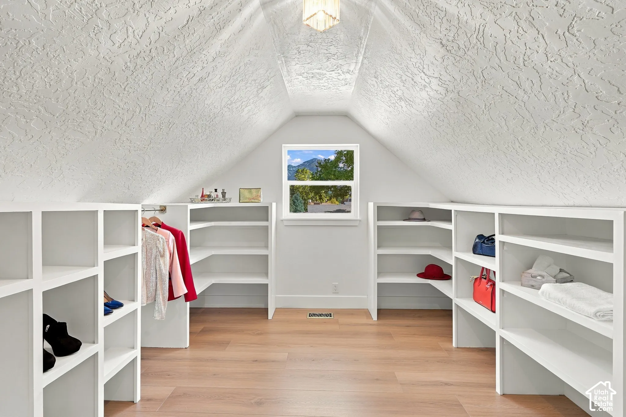 Primary walk-in closet with built-in shelving and hanging rods with wood-finish flooring