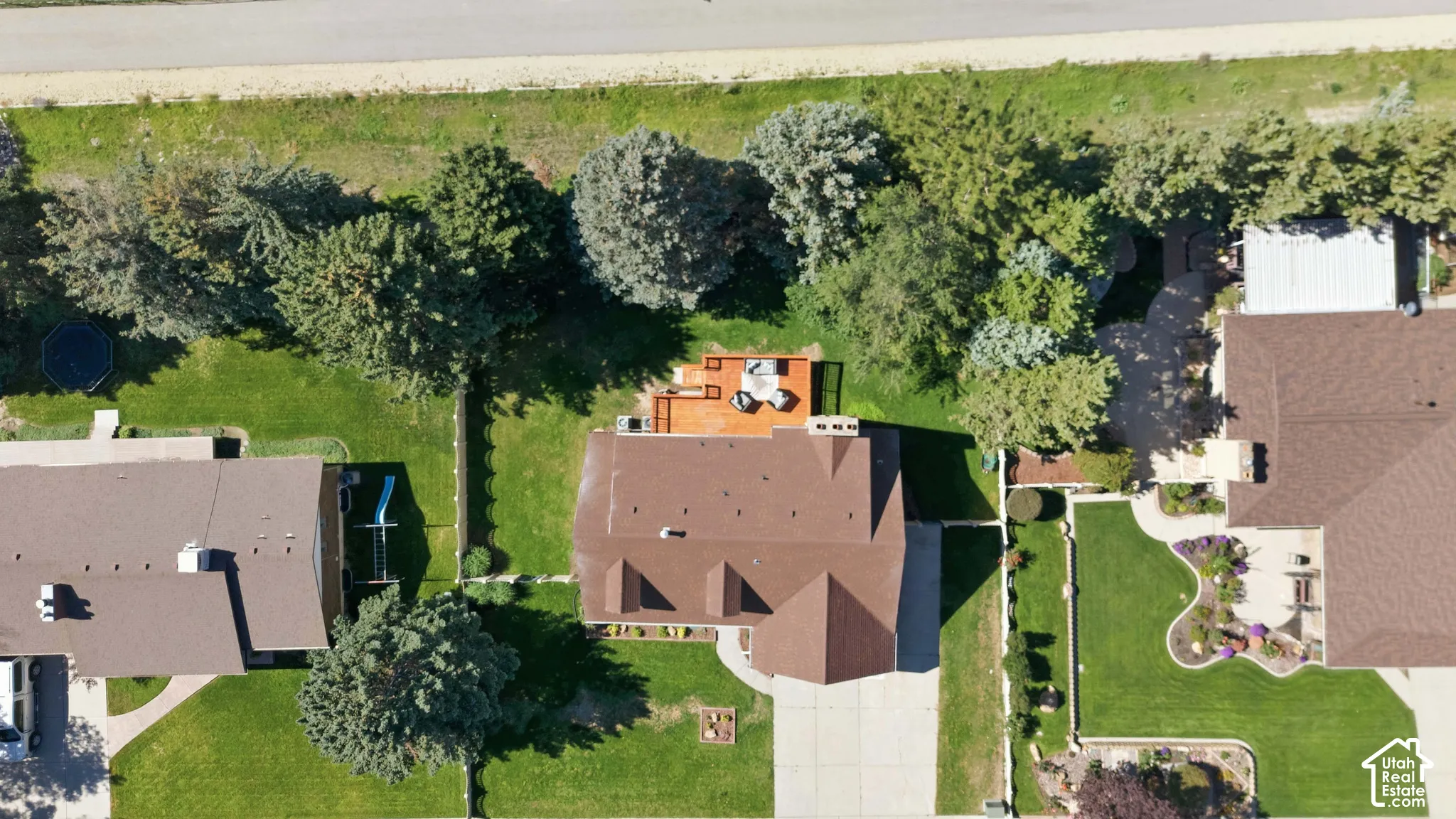 Expansive property featuring a brown shingle roof, a large wooden deck, mature trees, and manicured lawns