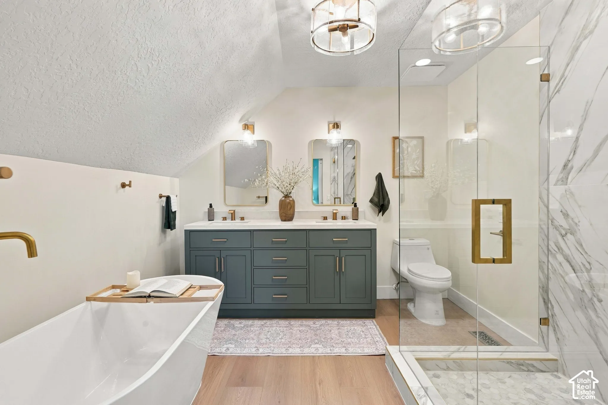 Spa-inspired primary bathroom featuring a freestanding soaking tub, dual-sink vanity with soft-close cabinetry in deep teal finish, marble-look tile surround, and a frameless glass-enclosed shower
