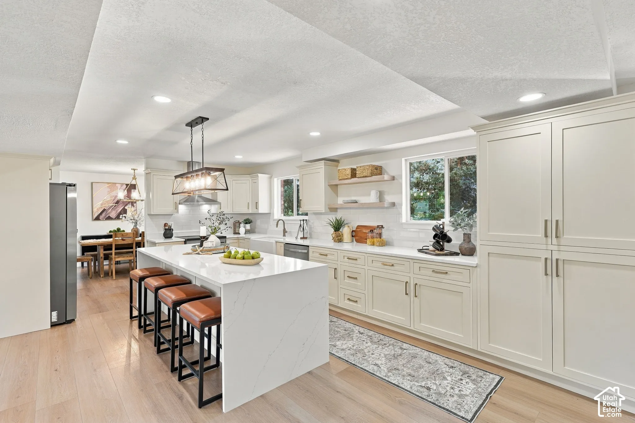 Spacious kitchen featuring an expansive central island with a waterfall countertop, light-toned cabinetry, stainless steel appliances, and wood-finish flooring