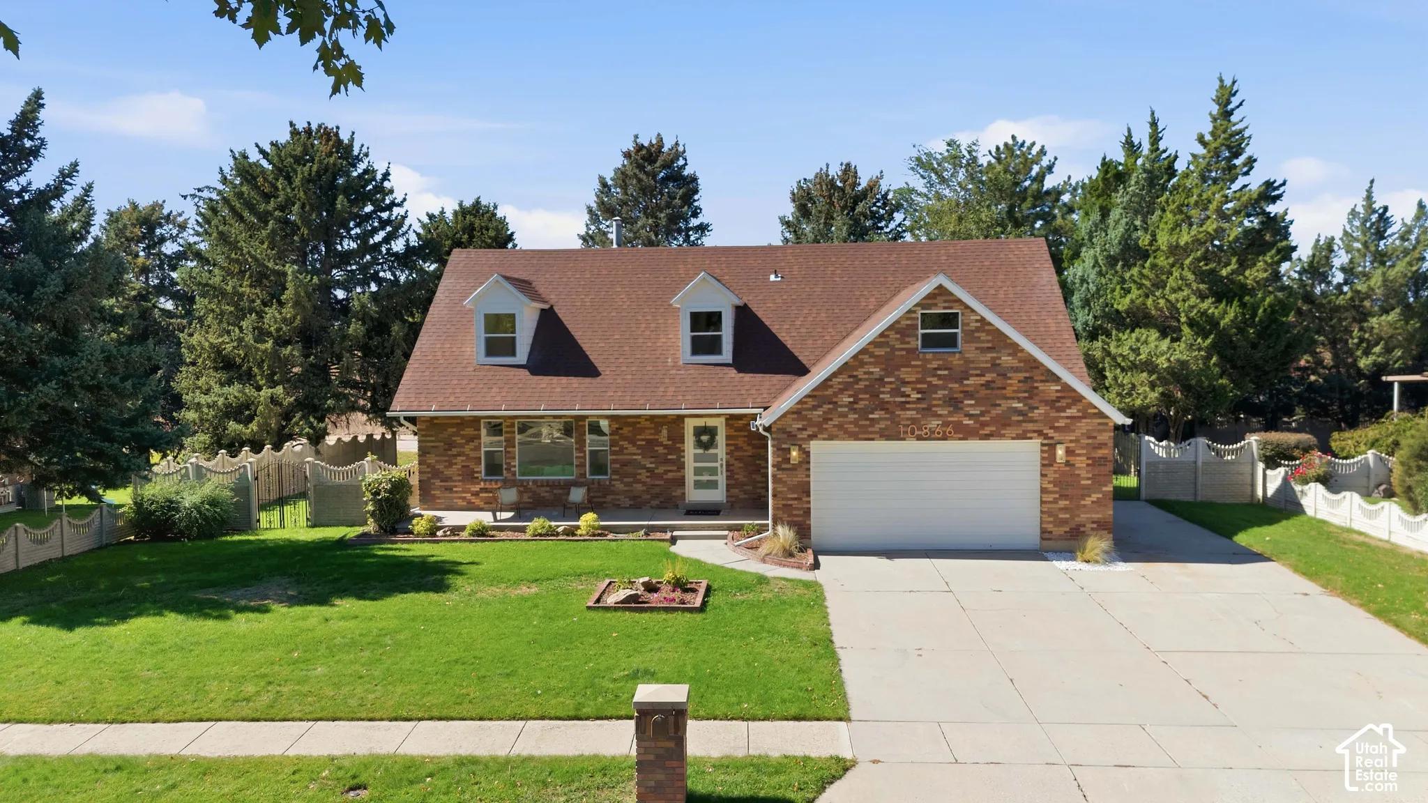 Brick exterior with dormer windows, attached garage, concrete driveway, and mature landscaping