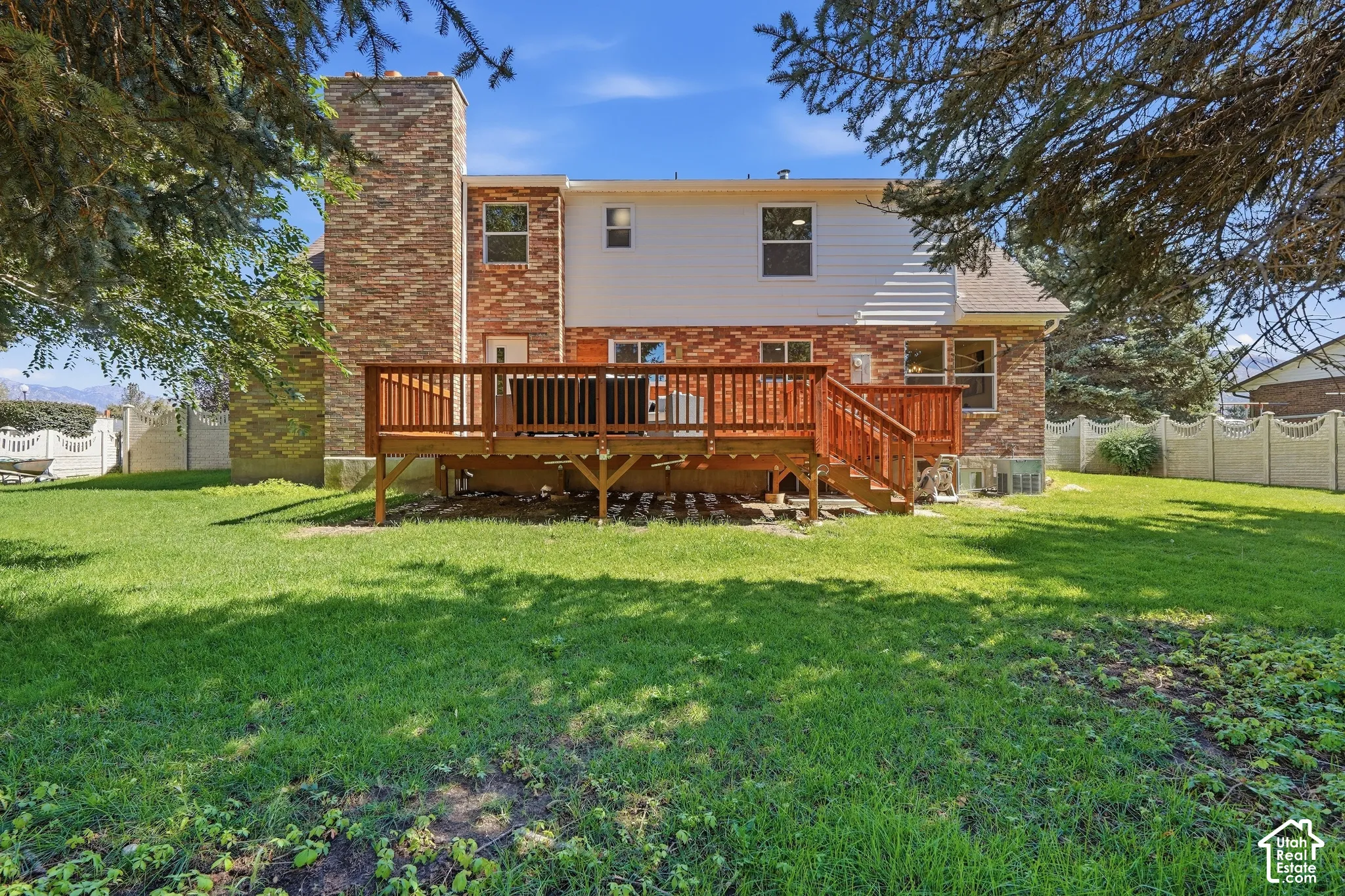 Expansive backyard featuring a manicured lawn, multi-level wood deck, and brick exterior with white siding