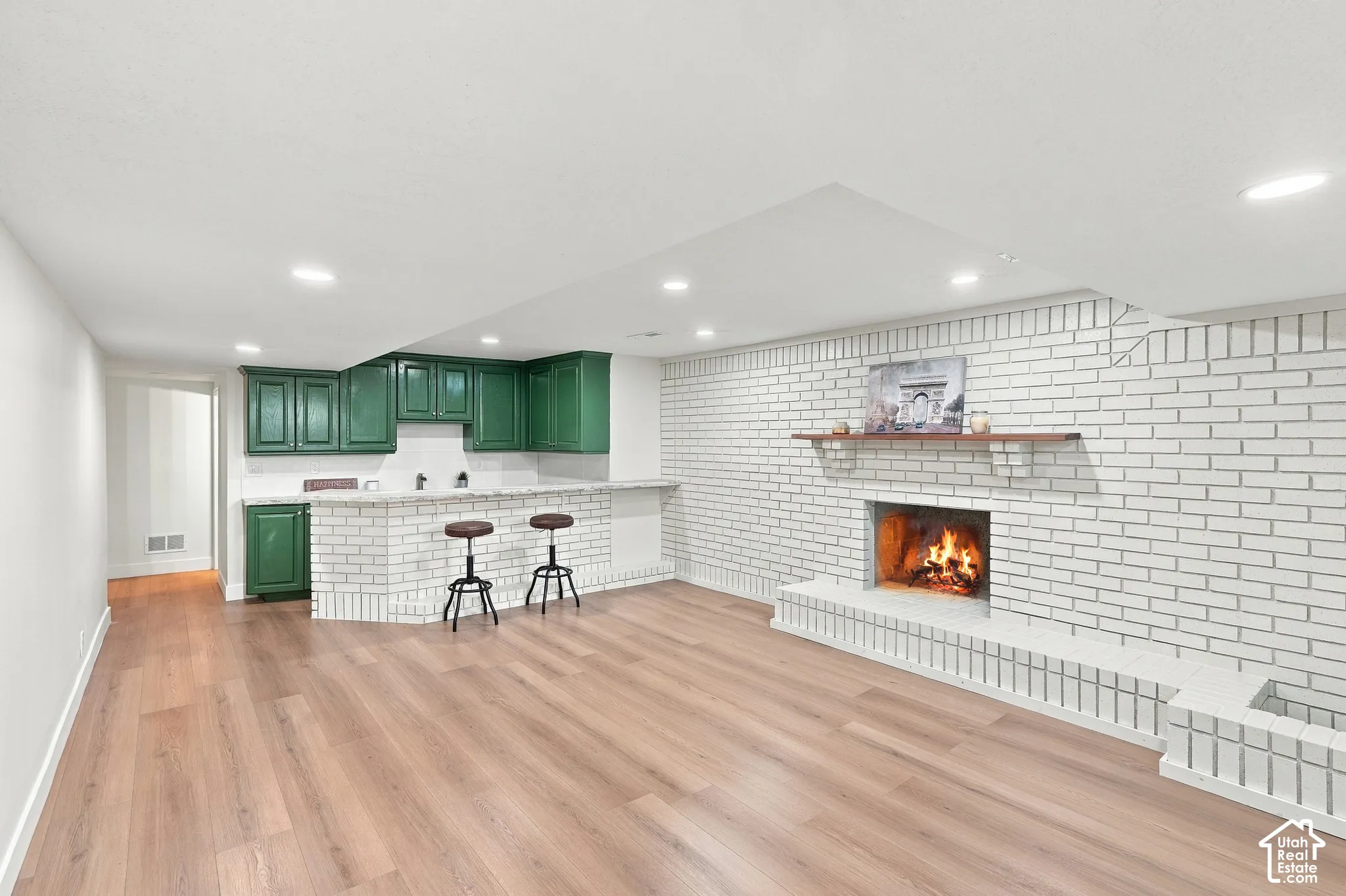 Wood-finish flooring, recessed lighting, and a white brick fireplace with a wood mantel