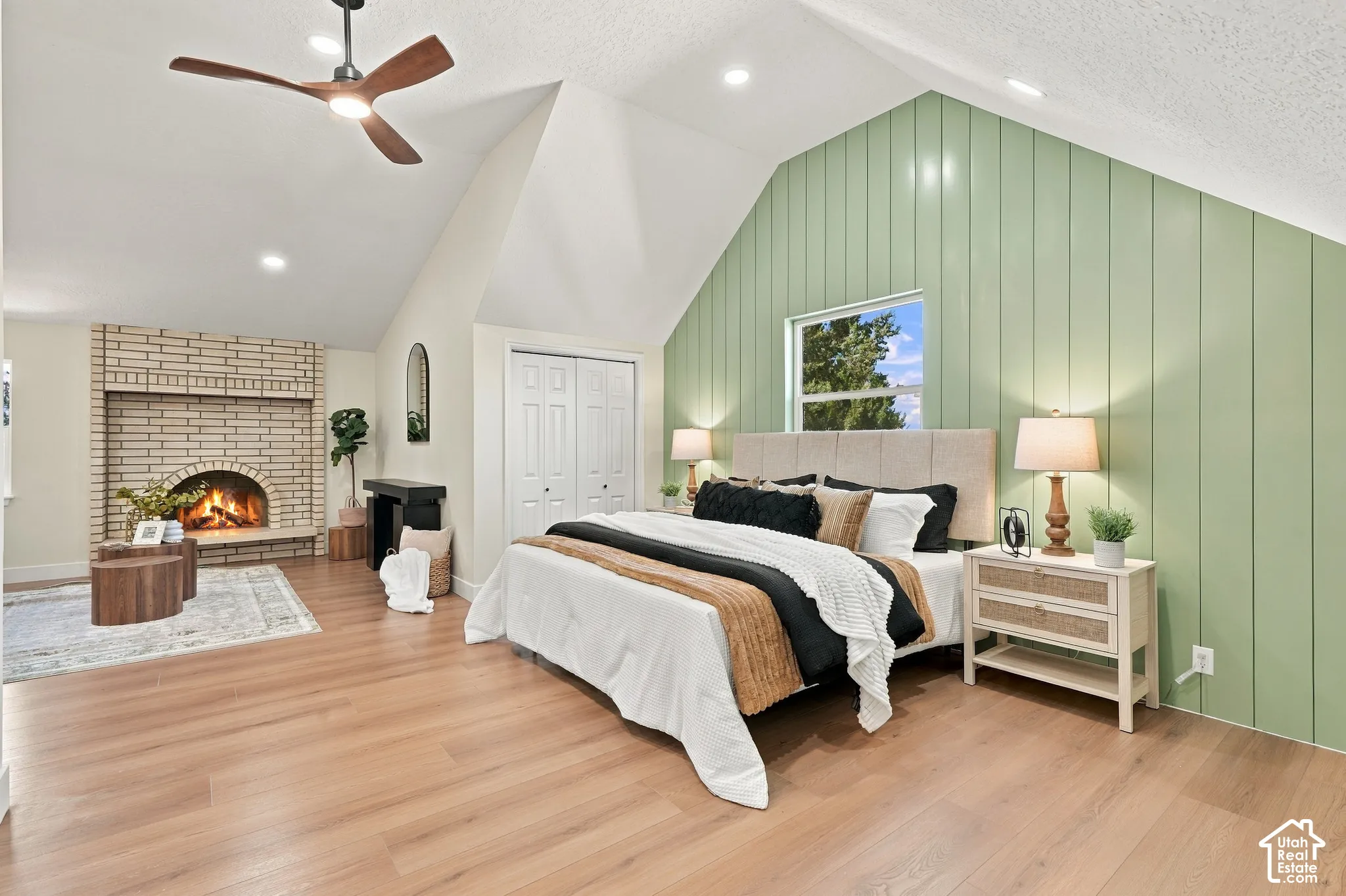 Vaulted ceiling with an integrated ceiling fan, wood-finish flooring, and a brick fireplace