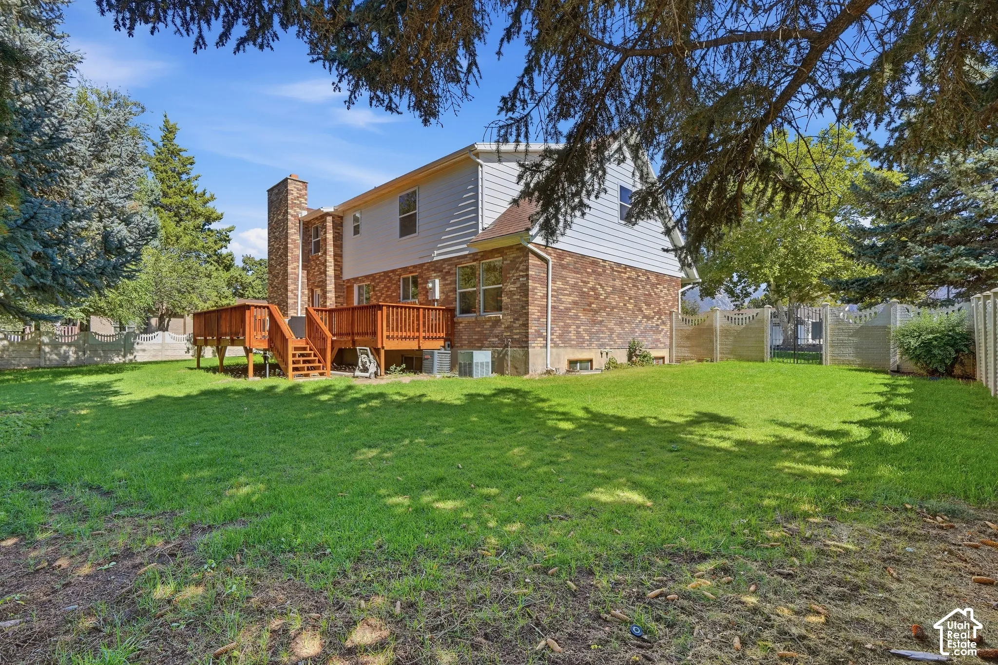 Expansive backyard featuring a multi-level wood deck, a brick exterior, and a large grassy area with mature trees
