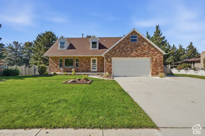 Brick exterior with dormer windows, attached garage, concrete driveway, and front lawn with mature trees