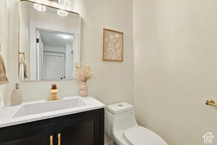 White integrated sink with gold-finish faucet, dark wood-finish vanity with gold-finish hardware, rectangular mirror with gold-finish frame, and wall-mounted vanity lighting