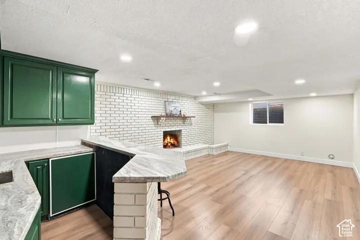 Wet bar with green cabinetry and stone-finish countertops, brick-finish fireplace with wood mantel, wood-finish flooring, and recessed lighting